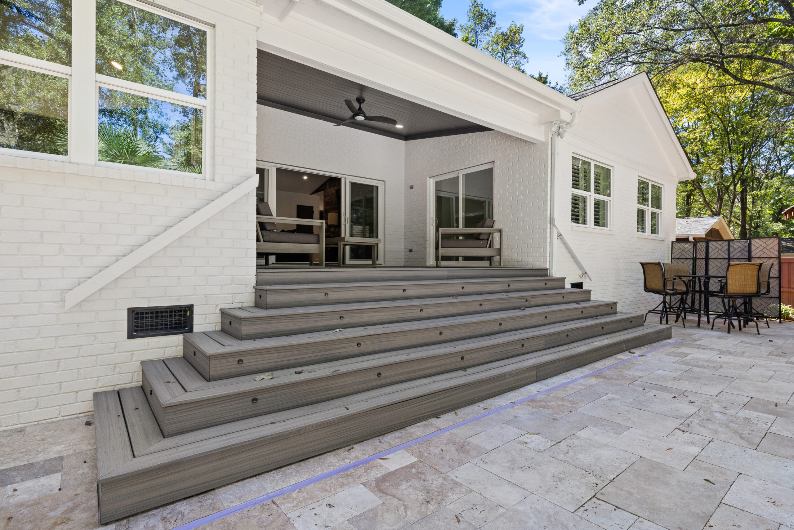 Wide grey steps leading from a white brick house down to a remodeled tiled patio