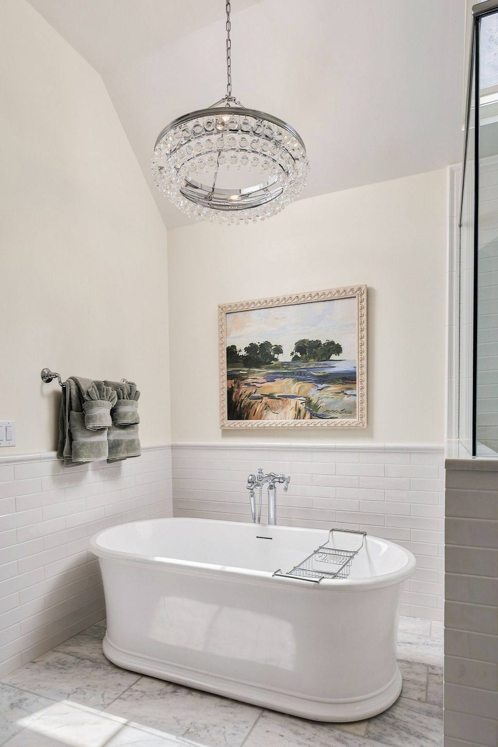 White freestanding bathtub beneath a crystal chandelier with folded towels on a rack
