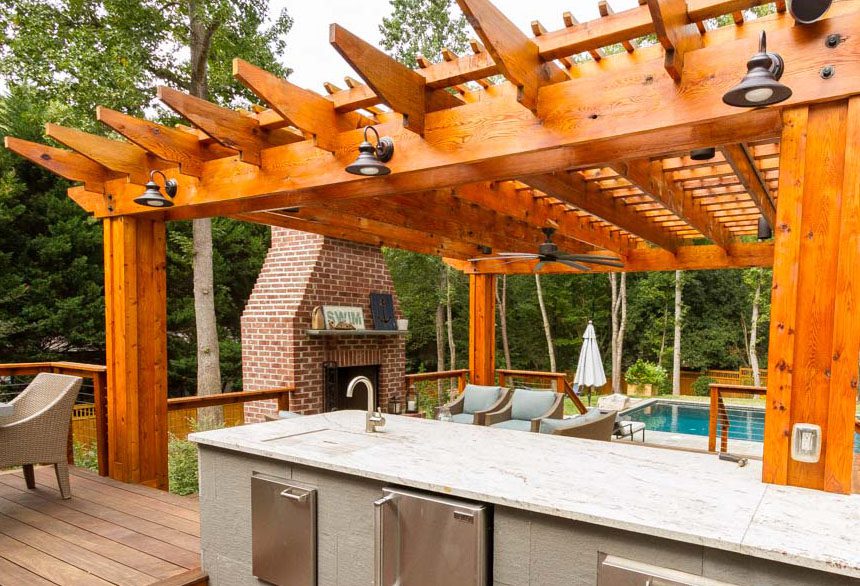 Wooden pergola with ceiling fans above an outdoor kitchen and seating area