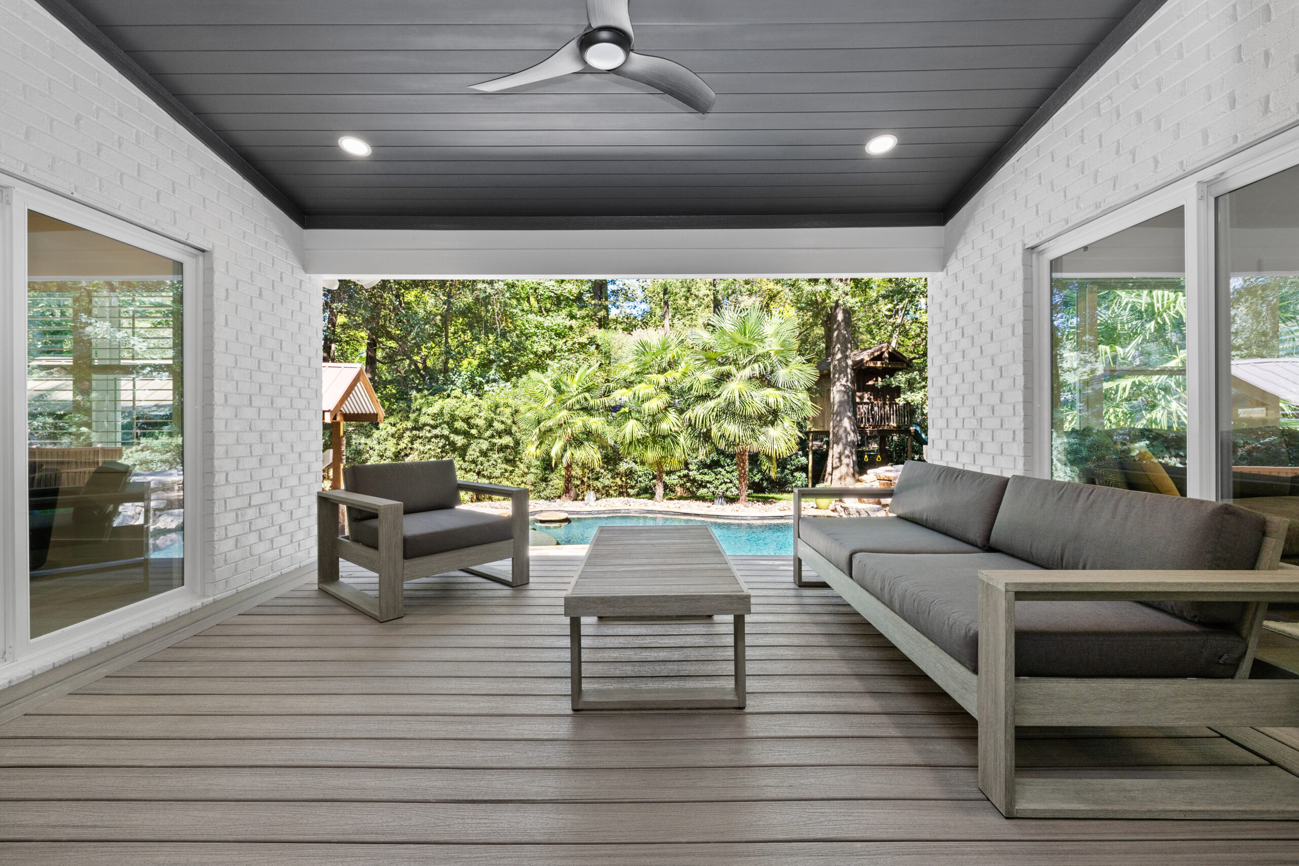 Modern covered patio with grey outdoor furniture, wood-look flooring, a ceiling fan and a pool view