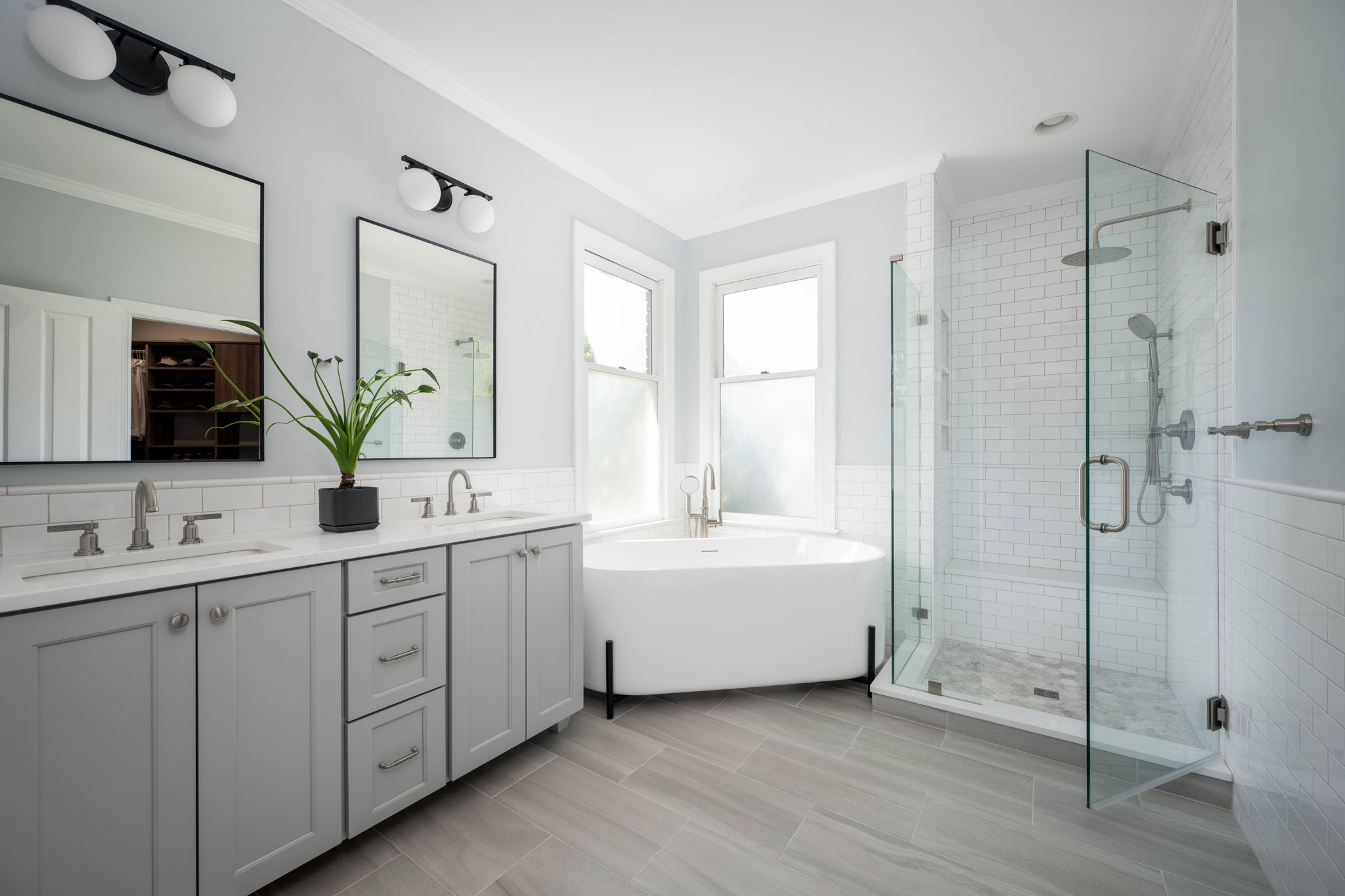 Remodeled bathroom with a glass shower, freestanding tub, grey double vanity and a large mirror